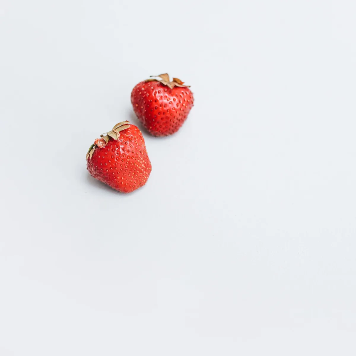 Two red strawberries on a white surface