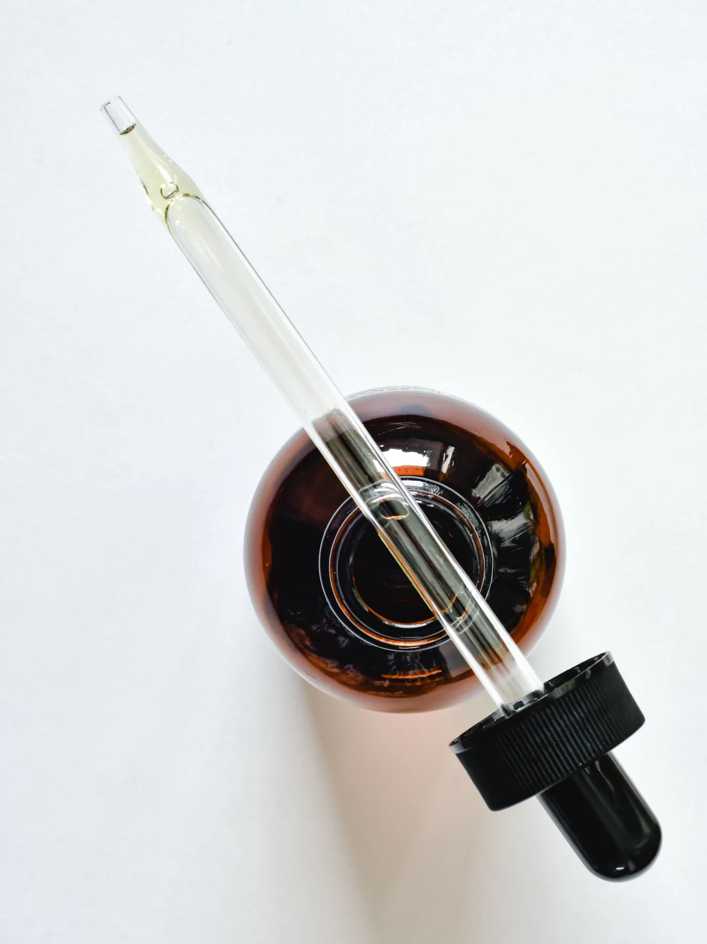 A glass dropper resting across an amber bottle, seen from above